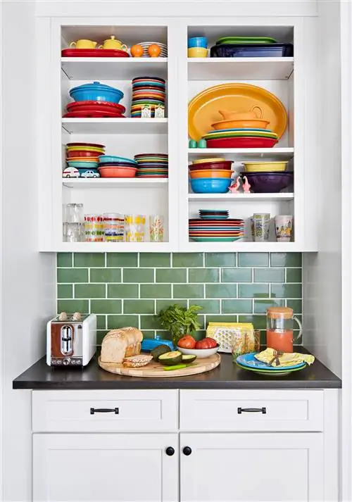 крупный план белых кухонных шкафов с посудой на полках, черной столешницей и фартуком из зеленой плитки метро