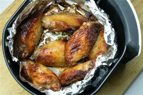 Фритюрница с алюминиевой фольгой и приготовленными куриными крылышками Фритюрница с алюминиевой фольгой и приготовленными куриными крылышками