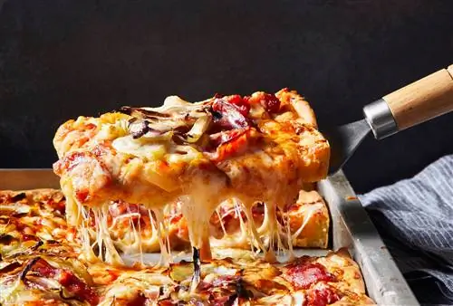 кусок пиццы поднимают со сковороды с завитками сыра