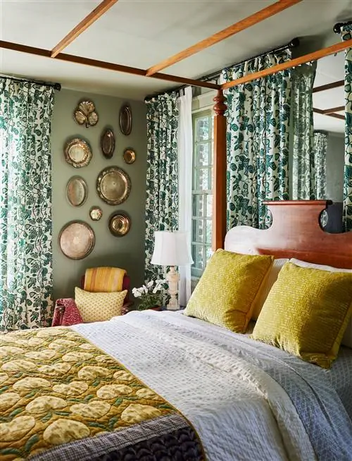 максимальная спальня с желтым узорчатым стеганым одеялом и занавесками с узором в виде листьев с латунными пластинами, висящими на стене