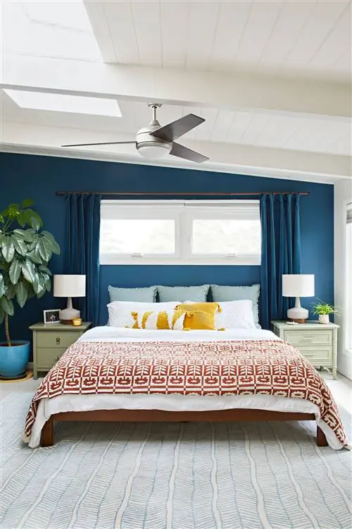 спальня с наклонными синими стенами, соответствующими синими шторами и большой кроватью
