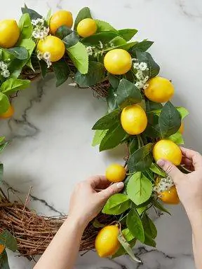 женщина кладет ветки лимона на венок из виноградной лозы