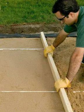 мужчина использует 2x4 для стяжки песка