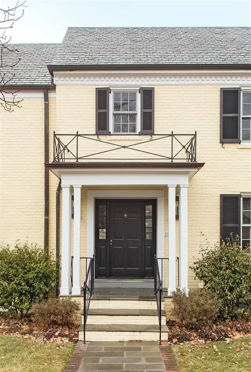 маслянисто-желтый кирпичный фасад с черными ставнями и входной дверью