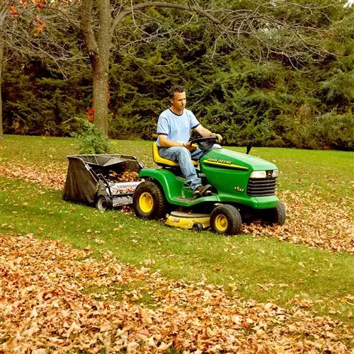 Человек собирает листья газонокосилкой