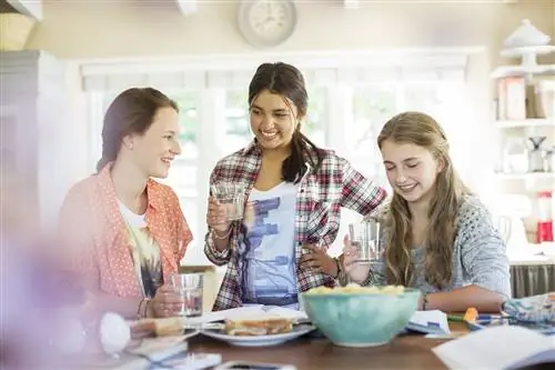 Три девочки-подростка пьют и едят за столом на кухне