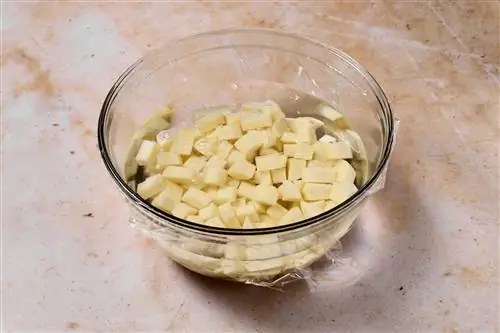 нарезанный картофель в стеклянной миске, покрытой полиэтиленовой пленкой