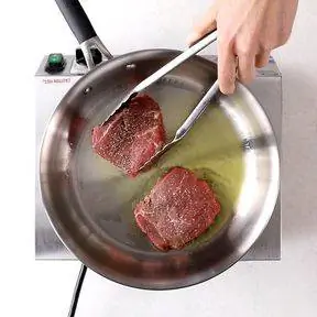 переворачивание обжаренного стейка на сковороде щипцами