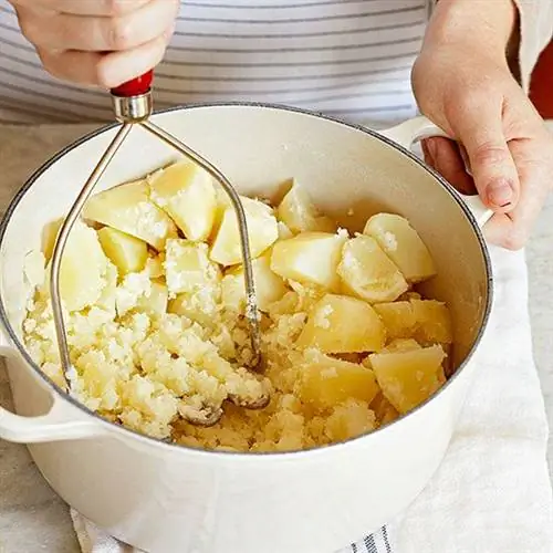 Картофельное пюре ручной толкушкой в белой кастрюле