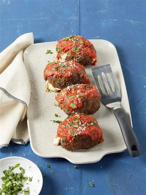 Мини-итальянские мясные рулеты, фаршированные сыром, на белом прямоугольном блюде с небольшим круглым блюдом из нарезанного базилика на переднем плане Мини-итальянские мясные рулеты, фаршированные сыром, на белом прямоугольном блюде с небольшим круглым блюдом из нарезанного базилика на переднем плане
