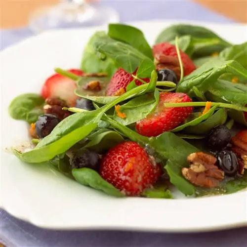 Салат из шпината и ягод с орехами на белой тарелке