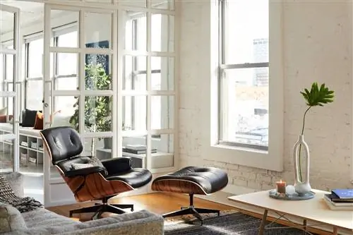 Кресло Eames с оттоманкой черного цвета и основанием из орехового дерева в стильной современной гостиной