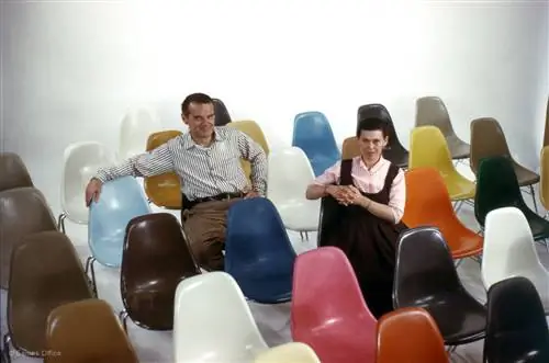 Чарльз и Рэй Имс сидят среди красочных стульев Eames из стекловолокна.