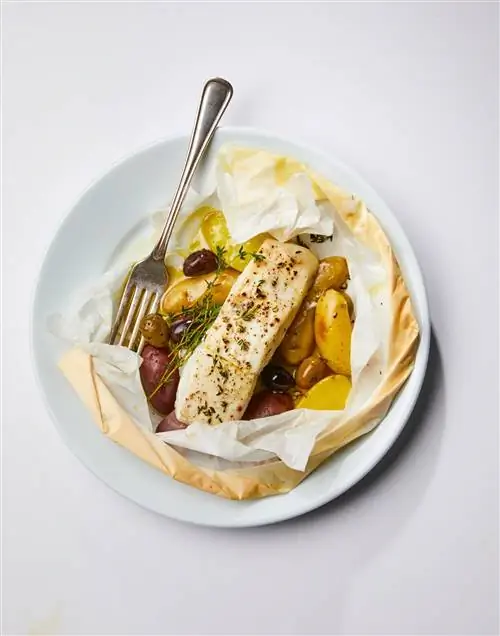 Запеченный в пергаменте палтус с тимьяном и оливками на тарелке с вилкой