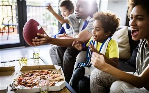 Этническая семья смотрит футбол по телевизору и ест пиццу дома