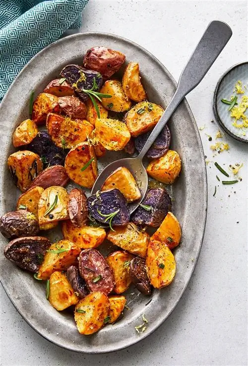 Картофель с розмарином и чесноком на сером блюде с ложкой и небольшим блюдом с цедрой лимона