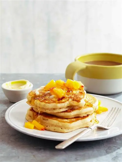 Пахта-персиковые блины с медовым маслом на белой тарелке с вилкой