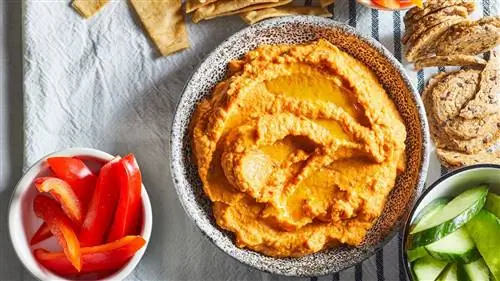 вид сверху на хумус с красным перцем, запеченный в тыкве, с овощами и питой