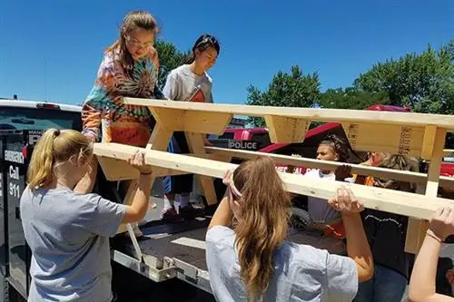 Группа девушек поднимает деревянный стол на трейлер