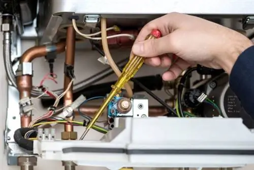 Техник ремонтирует комбинированный газовый котел с отверткой в руке Техник ремонтирует комбинированный газовый котел с отверткой в руке