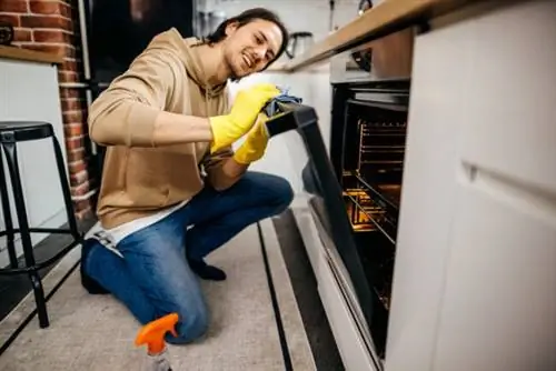 молодой человек моет верхнюю часть дверцы духовки