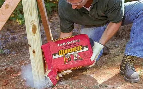 Мужчина заливает быстросхватывающуюся бетонную смесь Quikrete в отверстие для столба при строительстве забора.