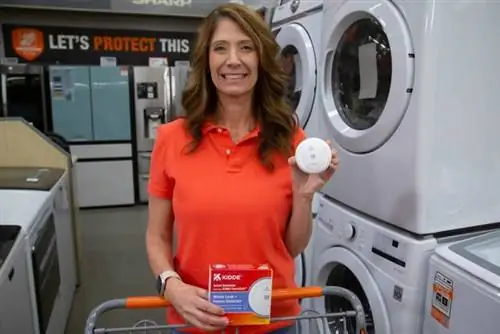 Джоди Маркс, ведущая программы «Лучший новый продукт» от домовладельца, держит детектор утечки и замерзания воды Kidde перед стиральными машинами в The Home Depot.