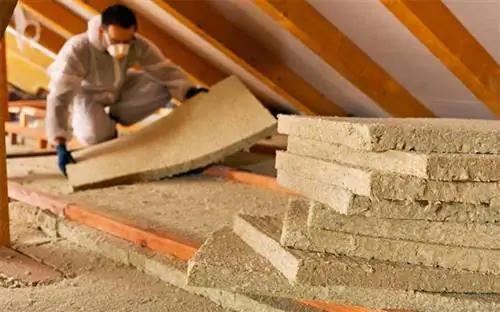 Мужчина в маске и перчатках при установке изоляции из минеральной ваты на чердаке