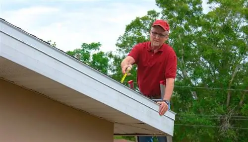 Мужчина на лестнице проводит проверку защиты от ветра на крыше