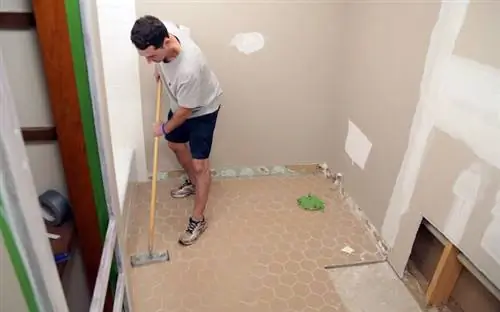 Мужчина использует шлифовальный станок для подготовки к укладке плитки на пол в ванной комнате.