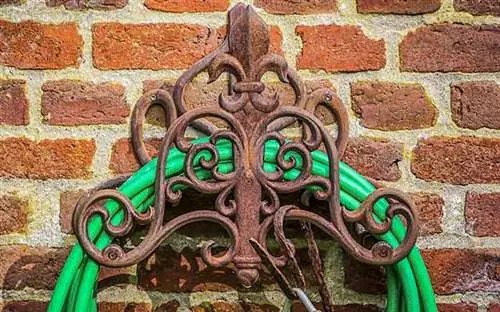 Кованый крюк для садового шланга, прикрепленный к стене кирпичного дома