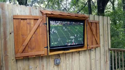 Футбольный матч на телевизоре с плоским экраном, размещенном в уличном шкафу для телевизора из дерева.