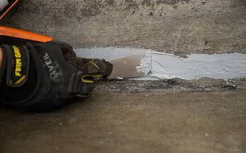 Рука в перчатке использует шпатель для выравнивания герметика Quikrete Advanced Polymer Concrete Crack Sealant.