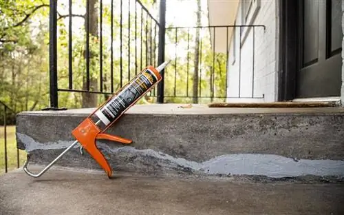 Пистолет для герметика, стоящий рядом с недавно заделанной бетонной трещиной, в пистолете для герметика.