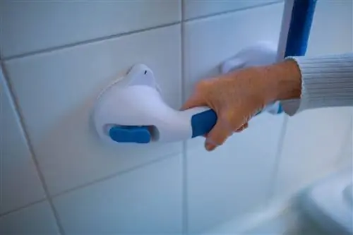Рука держит ручку с присосками на плитке в ванной.