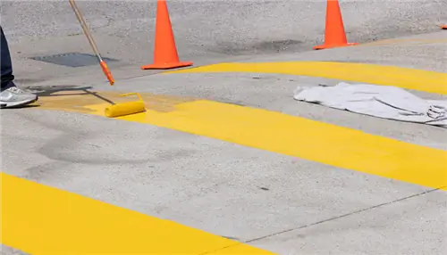 На этом изображении показан малярный валик, рисующий желтые линии на бетоне.