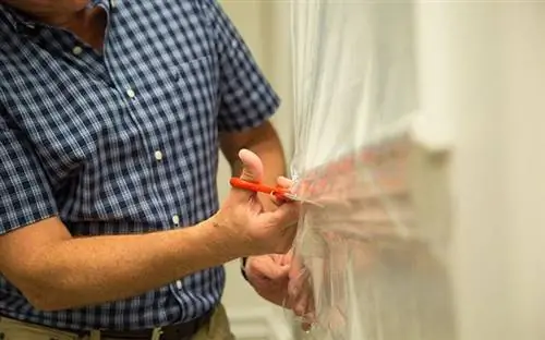 Сегодняшний хозяин домовладельца Дэнни Липфорд подрезает оконную пленку, пока он утепляет дом перед зимой.