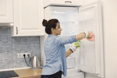 домовладелец моет полки в холодильнике тряпкой