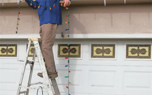 человек стоит на стремянке, чтобы повесить рождественские гирлянды