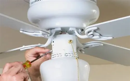 Крупный план руки с отверткой рядом с переключателем направления на потолочном вентиляторе