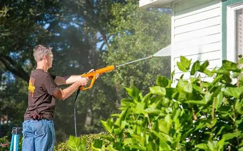 Мужчина моет под давлением виниловый сайдинг в доме