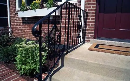 Черные кованые перила на крыльце кирпичного дома.