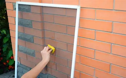 Мужчина моет оконные сетки мокрой губкой в руке