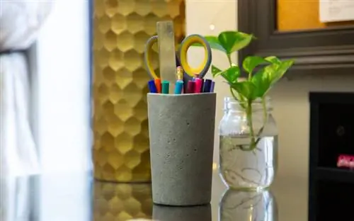 Крупный план офиса с бетонной чашкой для ручек, наполненной ножницами и ручками.