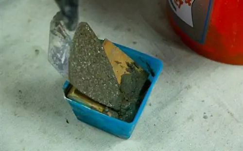 Рука в перчатке мастерком по кладке укладывает вторую заливку бетонной смеси поверх выреза из дерева.