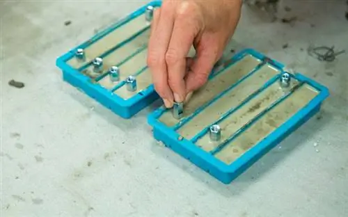 Крупный план руки, кладущей соединительные гайки в лоток для льда, наполненный бетонной смесью