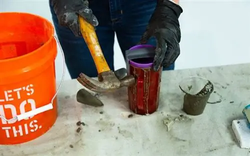 Рука в перчатке стучит по пластиковой бетонной форме резиновым молотком.