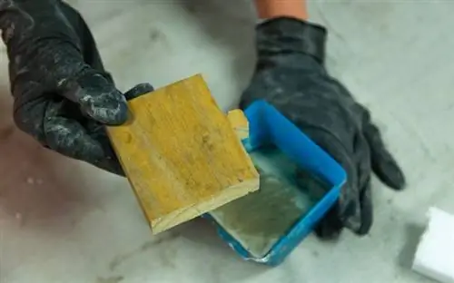 Каждый домашний офис должен быть спроектирован с учетом функциональности, включая место для отдыха смартфона. Рука в перчатке готовится поместить вырез из дерева в пластиковую бетонную форму.