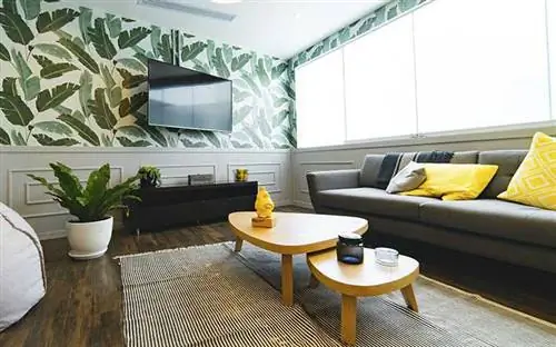 Гостиная с деревянными полами, ковровым покрытием, журнальным столиком, обоями с растениями, растениями в горшках и телевизором с плоским экраном над консолью.