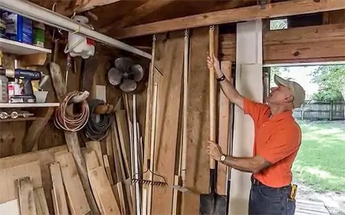 Джо Труини вешает садовые инструменты на потолочные балки своего сарая.